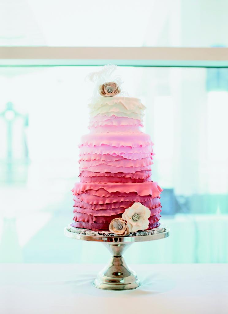 SHADES OF SWEET: Sunny Park Cakes dressed the ombré confection in ruffles and sugar paste flowers to mimic the bodice design and rhinestone belt of Ruth’s gown. Wrapping the cake plate in fabric added a colorful touch of pattern to the mix.