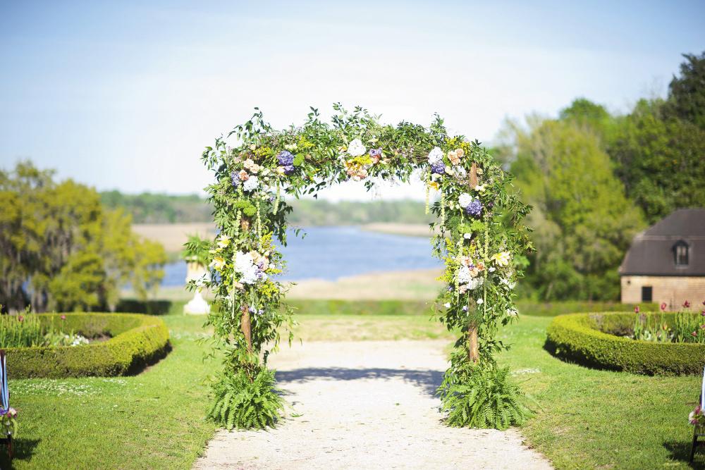 FRAMEWORKS: For an altar in keeping with the rainbow-hued palette of Casey Moore and Zach Tarrant’s Middleton Place nuptials, A Charleston Bride dressed a bamboo arbor in wild smilax, Spanish moss, pink and coral spray roses, white and blue hydrangea, purple lisianthus, yellow solidago, and more.