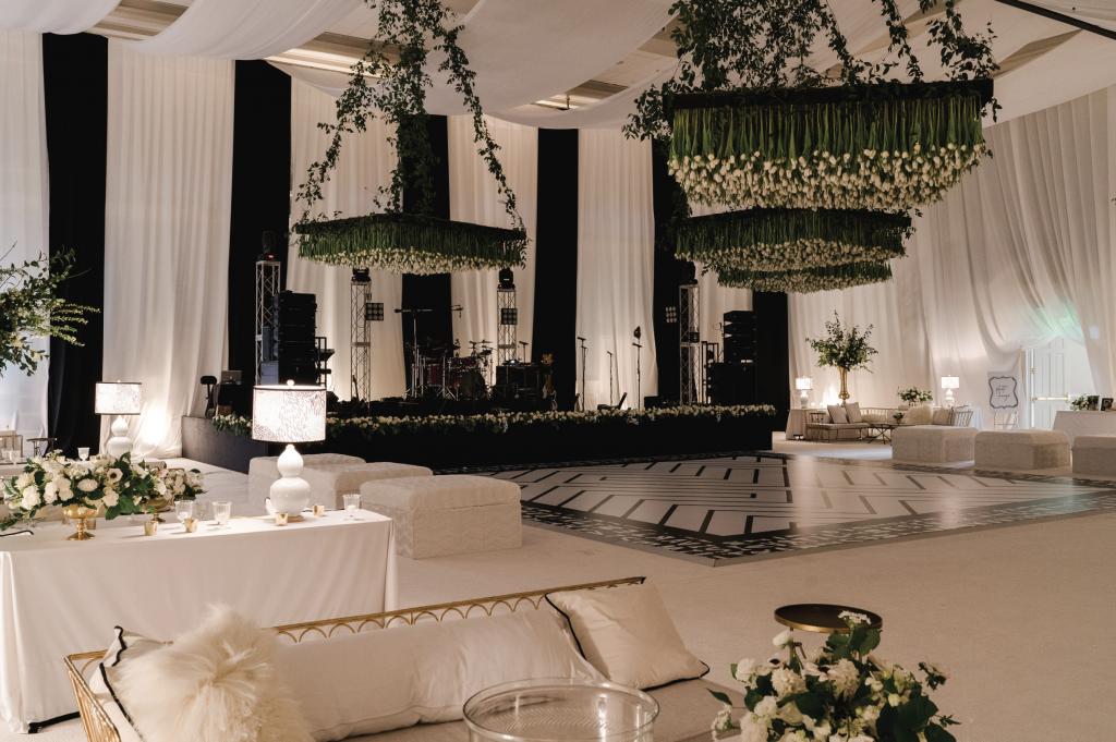 Against a canvas of white linens, cushioned seating, elegant lamps, and flower sprays, the striking entertainment space featured a black-and-white chevron dance floor that incorporated the pair’s initials into a personalized border design and was crowned by a suspended ceiling of upside-down tulips.
