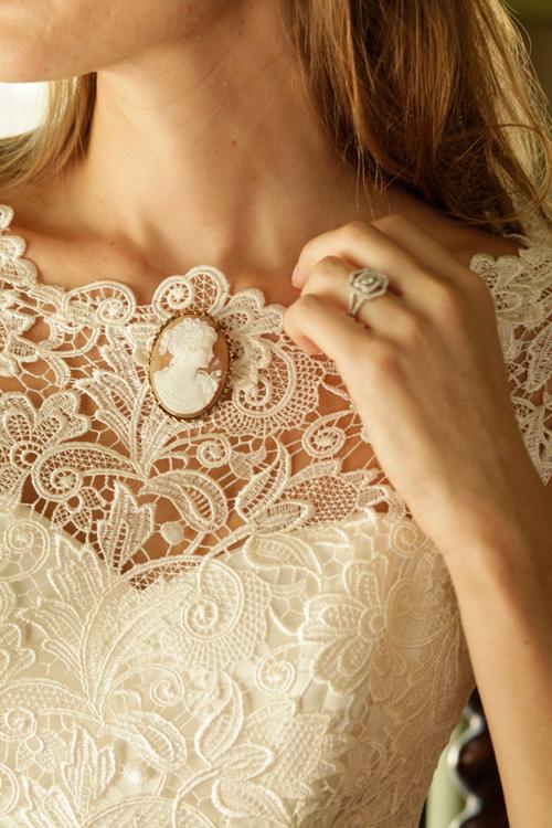 Callie Tein’s  “Nila” gown with bateau neckline, cap sleeves, and Italian lace overlay from Modern  Trousseau. Vintage cameo pin from Out of Hand.