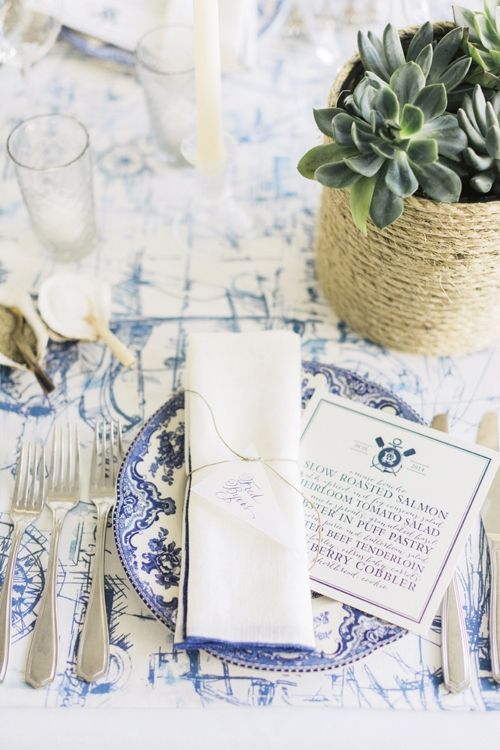 HAVE A SEAT: A runner printed with ships and compasses offered a maritime backdrop for blue-and-white china, napkins edged in royal blue, and mini burgee-flag place cards calligraphed by Elizabeth Porcher Jones.