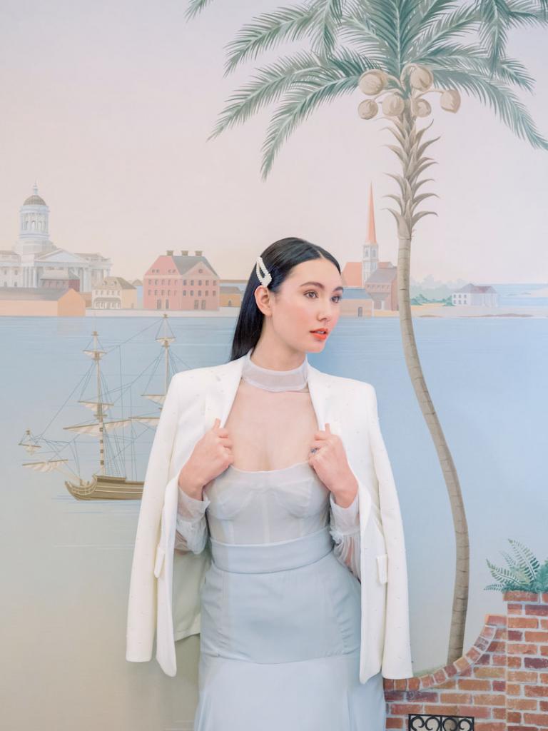Silk crepe gown in blue with hand-dyed tulle blouson, both from Emily Kotarski Bridal. Akris punto’s studded blazer from Gwynn’s of Mount Pleasant. Aquamarine ring from Diamonds Direct. Stylist’s own pearl clip. Mural by Julie Biskin