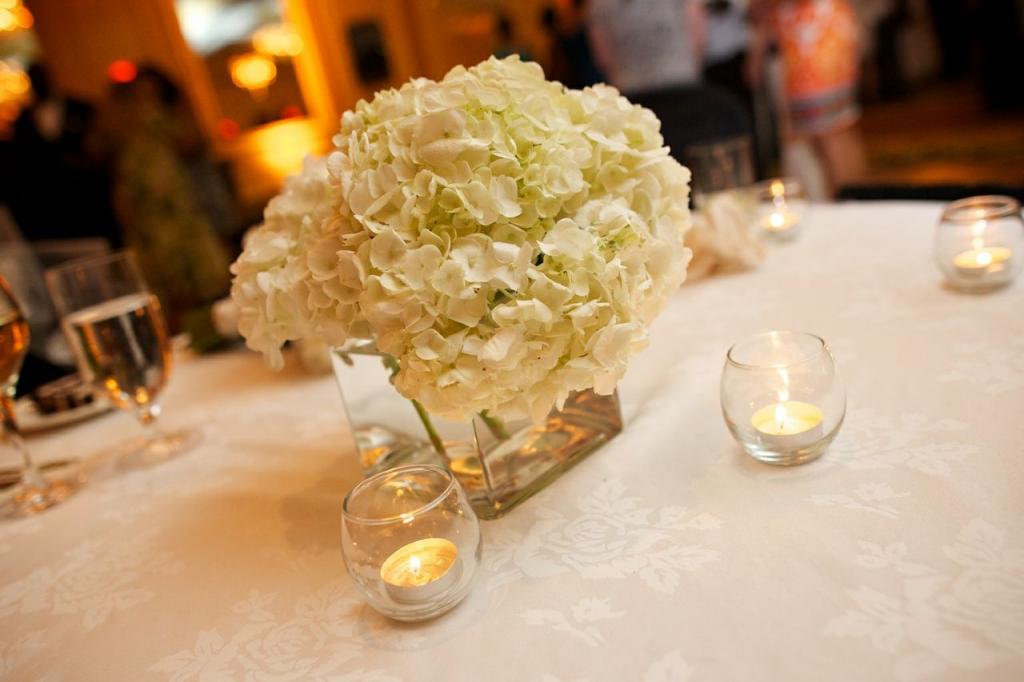 QUIET FLORA: White-on-white floral-pattern linens, hydrangea bunches, and votive candles kept reception tabletops soft and simple.