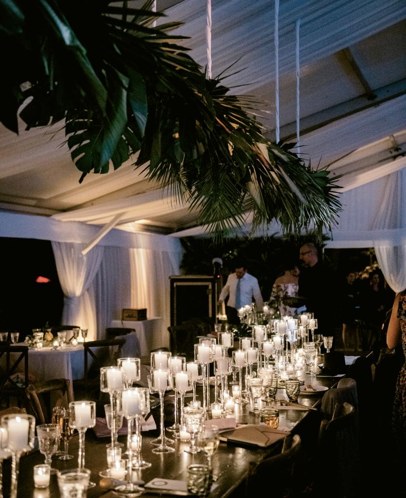A peek at Lucy’s wedding  Pinterest board (@LDietch) tells the tale of what inspired the couple’s reception. Pin after pin populated with tropical installations and accents led to a tent dressed in leaves—Monstera, caladium, areca, and hosta—fern fronds, and more. Saved images of candlelight tabletops on her board evoke a club-slash-restaurant vibe while strands of café lights twinkle in merriment.