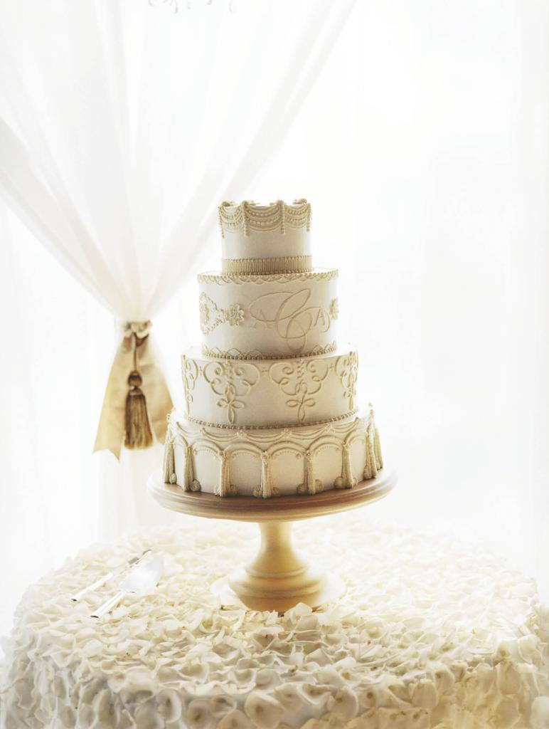 ICED, ICED, BABY:  This towering treat from Wedding Cakes by Jim Smeal was embellished with tone-on-tone patterns and the  couple’s monogram. “It was a work  of art on the outside and it tasted  fabulous on the inside!” says  the bride. Hundreds of ivory petals carpeted the table linen for a  decadent, delicate effect.