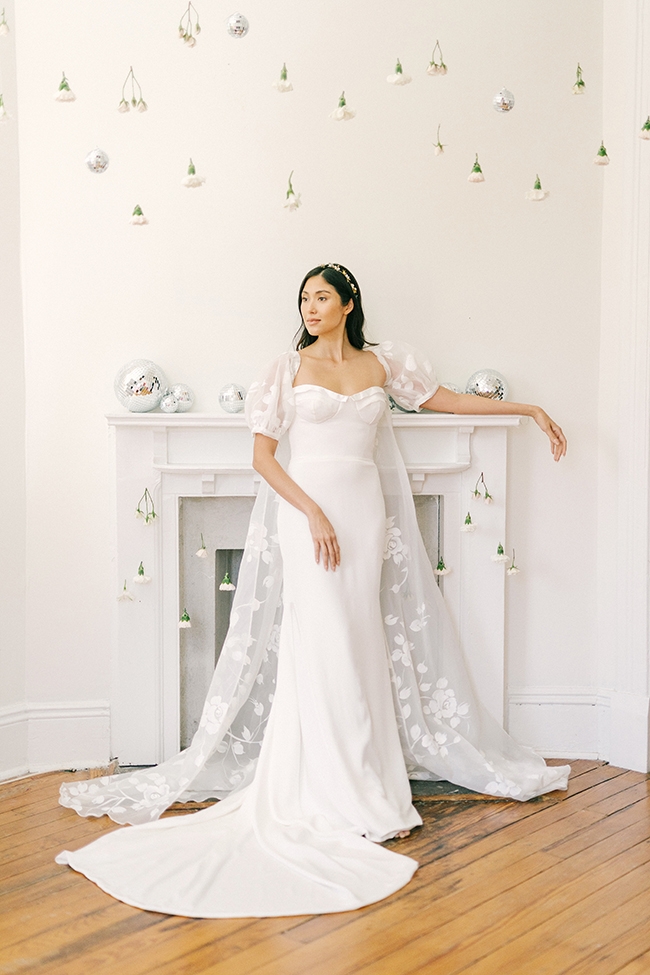Summer Elegance - “Lily” gown &amp;  “Coast” cape by  Emily Kotarski Why We Love It “We love the flattering lines of the silk corset, and the cape makes a bold fashion statement to complete the look.”  –Emily Kotarski, Emily  Kotarski Bridal