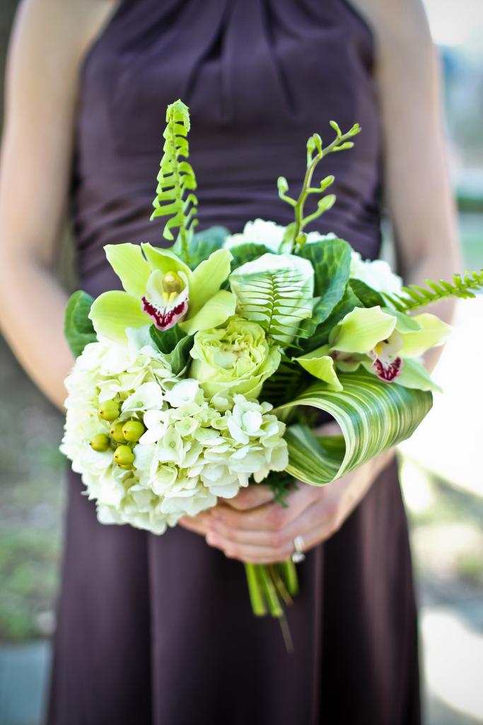 FRESH EFFECT: Jennigray Hewitt of RiverOaks mixed hydrangea, hypericum berries, large variegated ti leaf, and fern for an earthy green bridesmaid bouquet. Orchids added small pops of purple to coordinate with the attendants’ frocks.