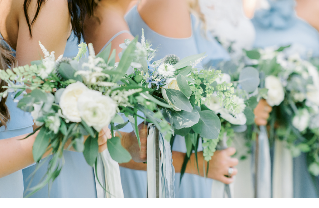 SYG Designs made bouquets dominated by greenery and dotted with blue and white blooms. Trailing ribbons that danced in the breezes added to the florals’ airy style.