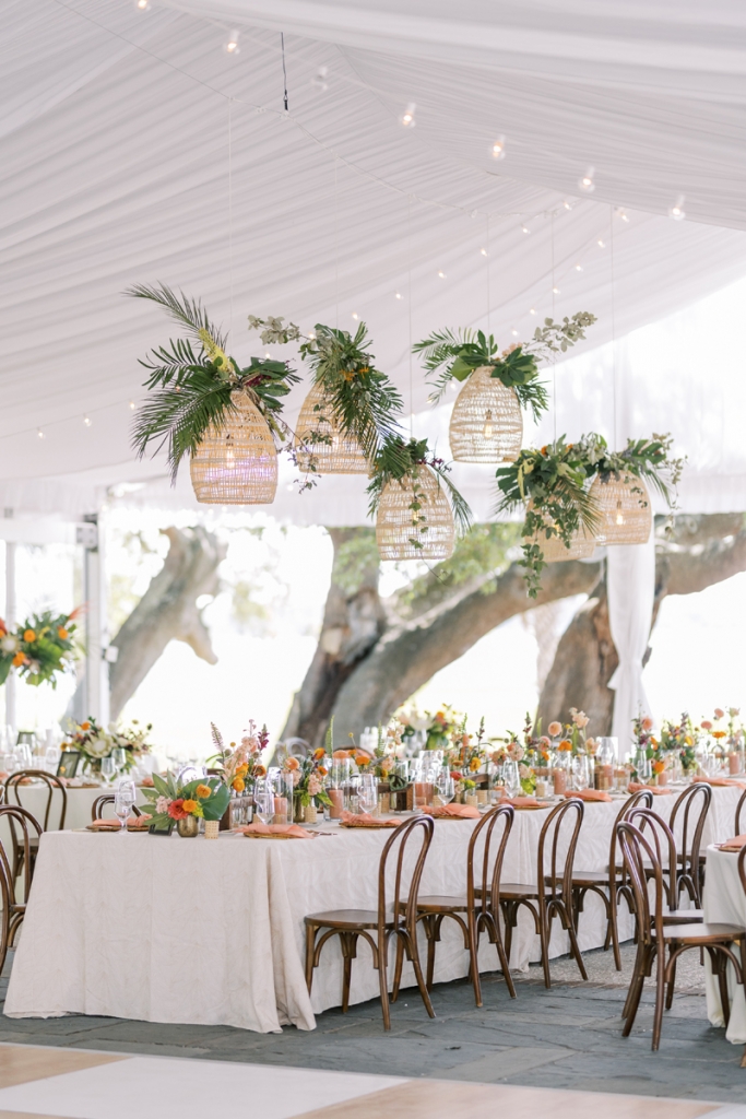 The big day’s tropical, boho-chic decor—inspired by a recent viewing of the first season of The White Lotus—was carried out through natural fabrics, abundant bright flowers, and hanging rattan lamps capped with greenery.