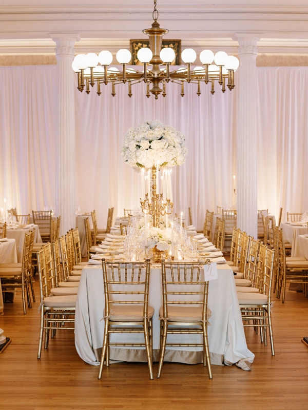 The reception’s gilded decor glistened against soft white blooms, draped linens, and Hibernian Hall’s Greek Revival architecture;.