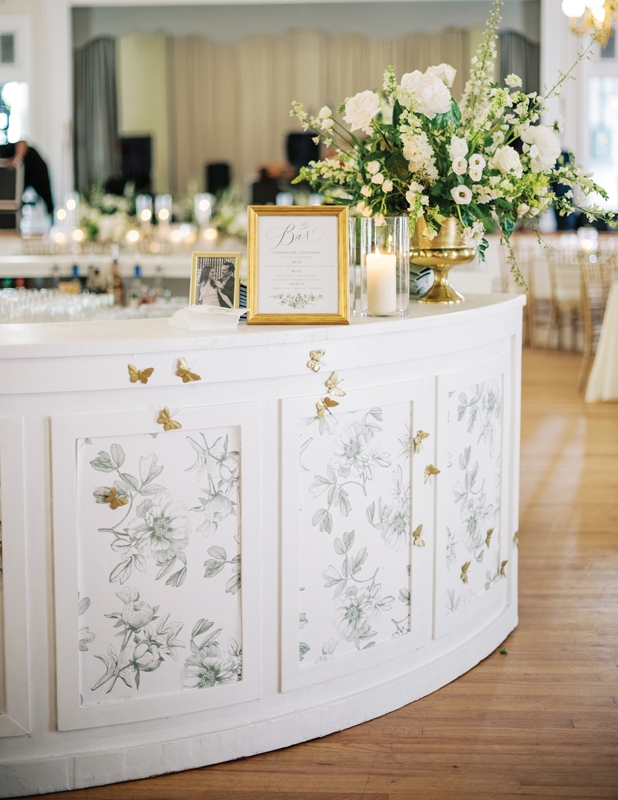 Anchored by a green-and-white palette, the reception featured design details like glowing glass hurricanes and the gold butterflies that decorated the bar, handpainted by the couple.
