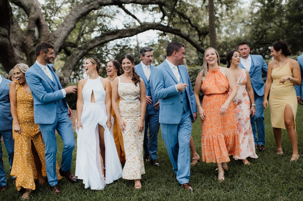 The wedding party’s palette popped against the venue’s regal riverfront, where the Bearded Florist wound technicolor blooms of safflower, spray roses, and gloriosa lily around knotty oaks.