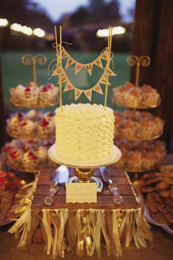 SIMPLY IRRESISTIBLE: &quot;Our couple&#039;s cake was so good we couldn&#039;t bear to leave it in the freezer for a year,&quot; says Ashton, &quot;so we ate it when we got back from our honeymoon!&quot; A cake topper banner accented the confection, while a note told guests it was only for the newlyweds. A garland of ribbons wrapped around a wooden crate took its dais from rustic to romantic.