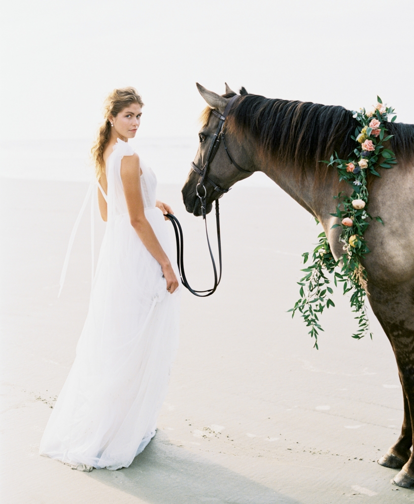 “Kendall” corseted tulle gown with pearl accents by Emily Kotarski Bridal. Pearl jacket earrings from Southern Protocol Bridal. Carolina Marsh Tacky pony, “Silky”, from Seabrook Island Club Equestrian Center. Florals by Out of the Garden. Location: Seabrook Island, Beach Access 6.  Photograph by Perry Vaile
