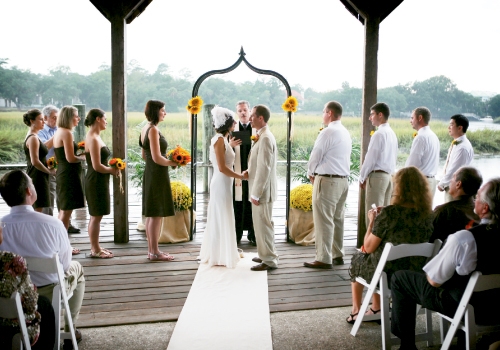 TWO IN ONE: Holding the ceremony and reception in the same location saved money. As for the view? “The beautiful marsh was definitely a focal point,” says Rheney. To add pops of color without competing with the surroundings, they tied two handfuls of sunflowers to the arbor with raffia, and flanked the structure with yellow mums in pots swathed in burlap.